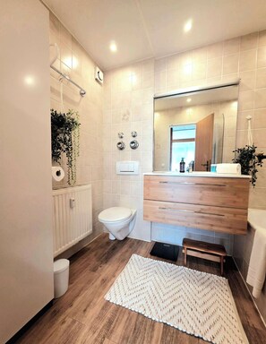 Une salle de bain moderne avec un meuble-lavabo en bois, des toilettes, une douche et un miroir.