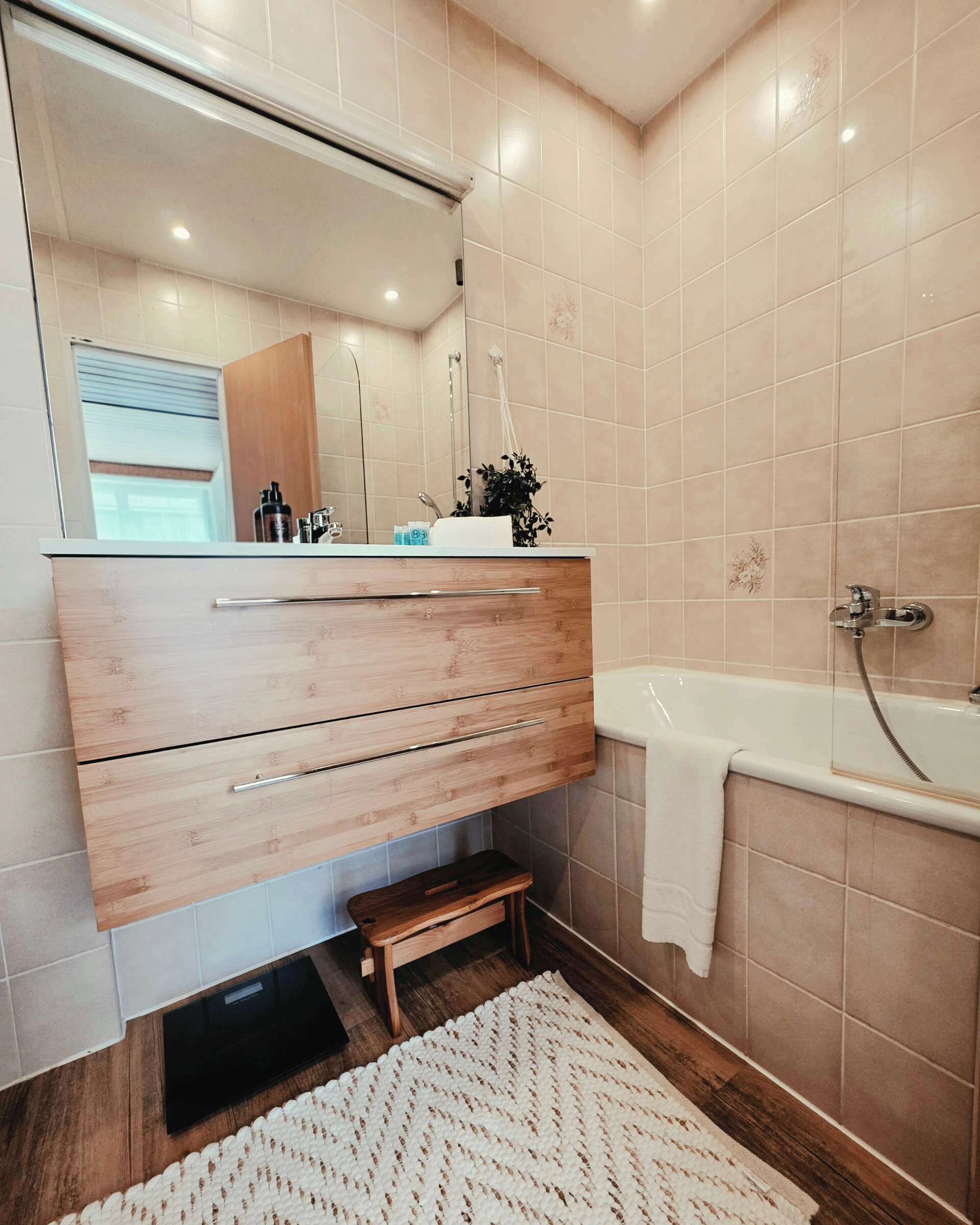 Ein Badezimmer mit einem Holzwaschtisch, einem Spiegel, einer Dusche und einer kleinen trittfesten Stufe.