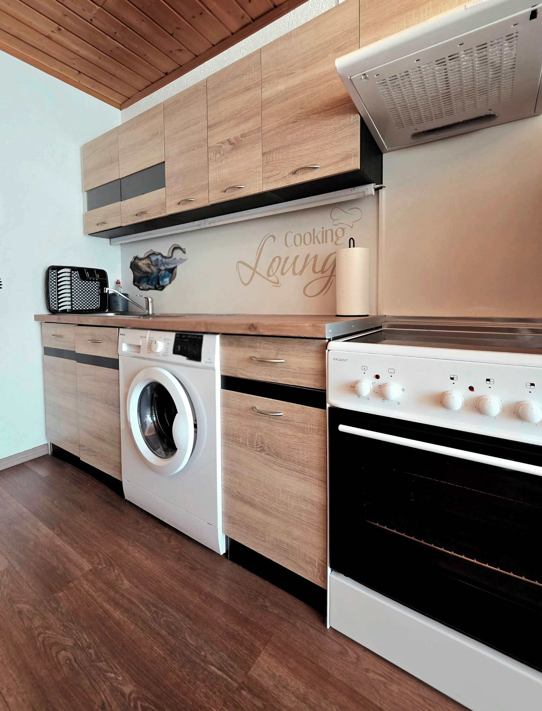 A modern kitchen with wooden cabinetry, a built-in washing machine, a stove, and a microwave.