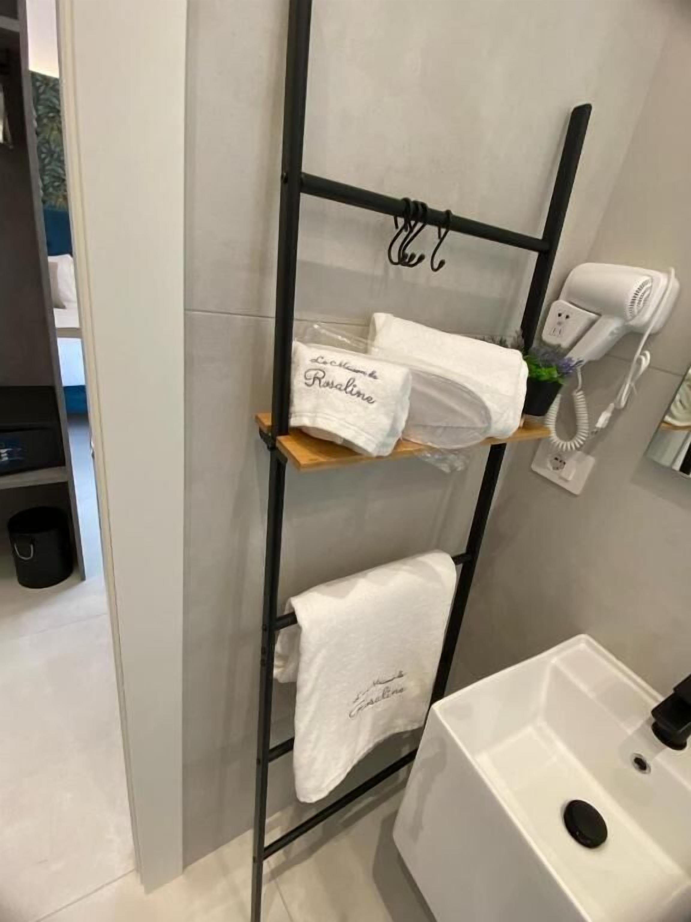 A bathroom with a glass shower enclosure, a white sink, a towel rack with a towel, and a hairdryer.