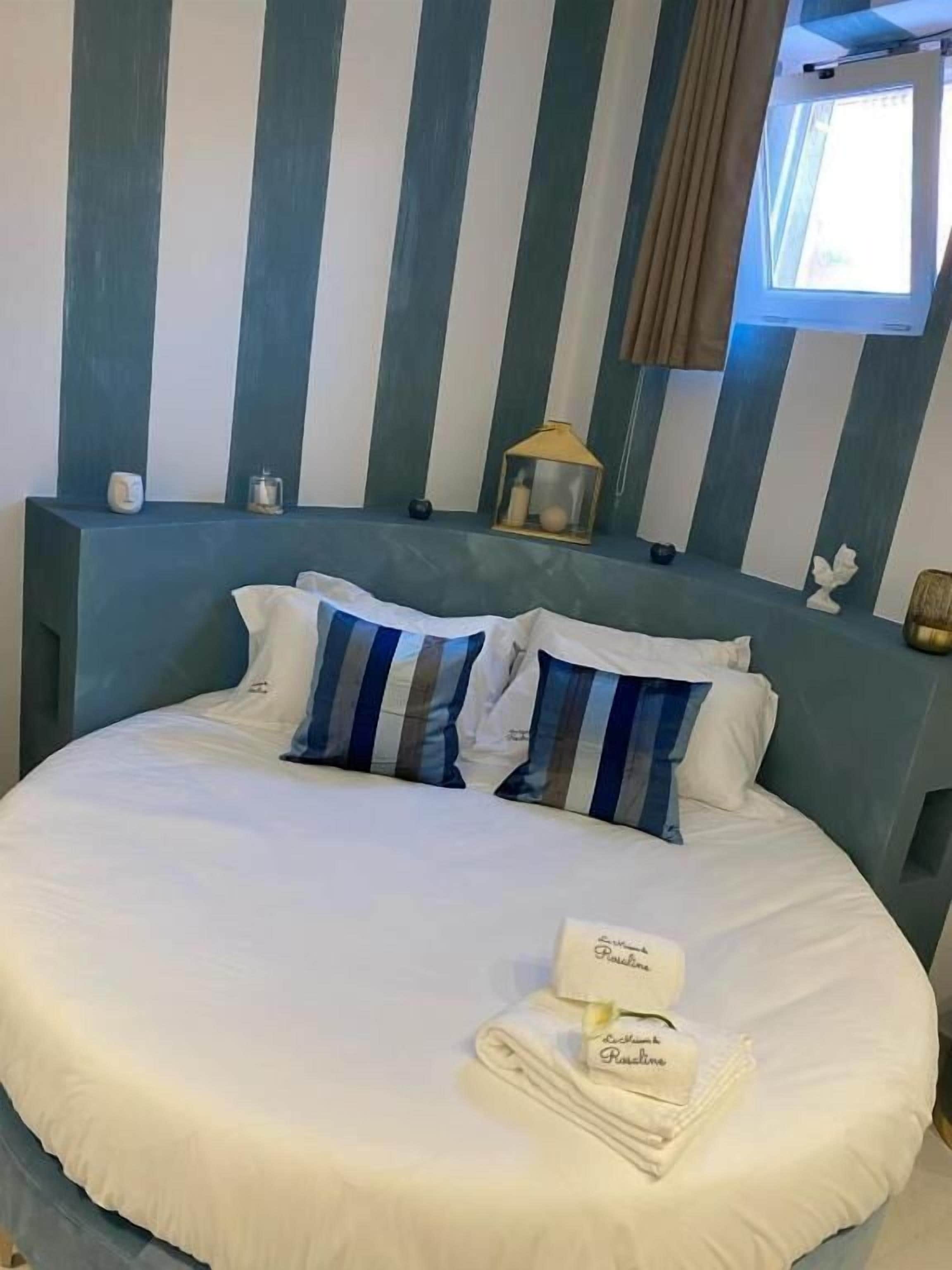 Un lit avec une couette blanche, des oreillers à rayures et une table de chevet sur laquelle se trouvent une lampe et un petit objet décoratif.