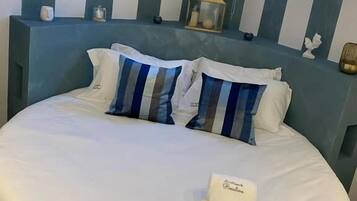 A bed with a white duvet, striped pillows, and a bedside table with a lamp and a small decorative item.