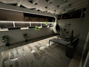 A room with a wooden floor, a bench, potted plants, and a window with a lighted ledge.