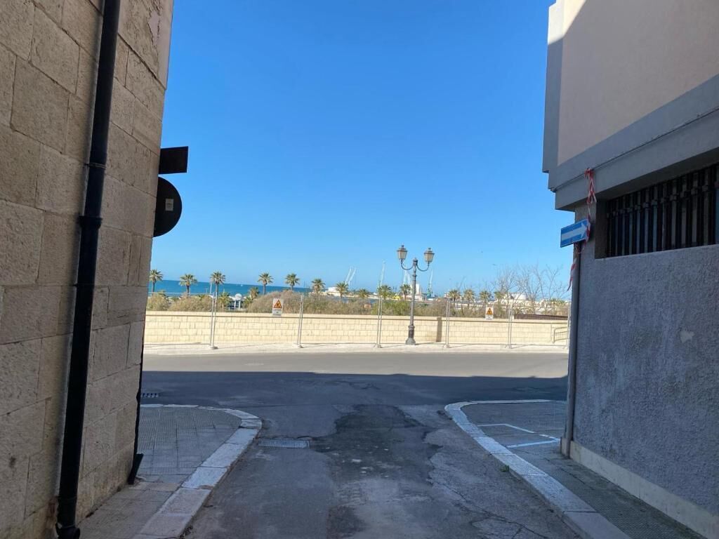 A street view with a clear sky, a road, and a distant view of palm trees and buildings.