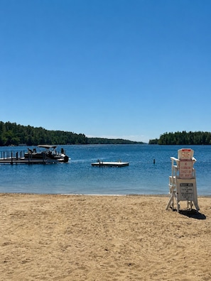 Une plage avec un panneau indiquant qu’il est interdit d’utiliser des bouées ou des gilets de sauvetage, un quai avec un bateau et une rive sablonneuse.