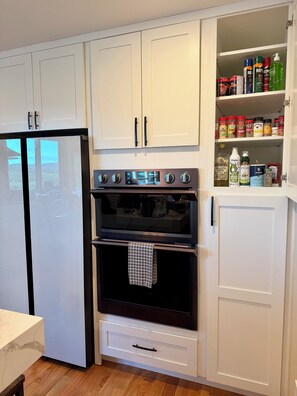 Una cocina equipada con refrigerador, horno y despensa con diversos alimentos.