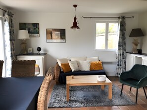 En stue med en sofa, et træbord, en grøn lænestol, en lampe og et vindue med gardiner.