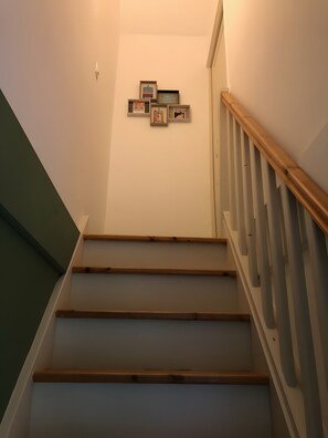 Un escalier avec des marches en bois et une rampe, menant Ă un palier oĂč sont accrochĂ©es des images encadrĂ©es au mur.