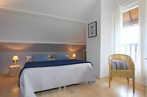 Et soveværelse med seng, sengeborde med lamper, en fletstol og et vindue med gardiner.