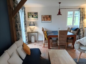 Kodikas olohuone, jossa on sohva, ruokapöytä tuoleineen, lamppu ja taideteoksia seinällä.
