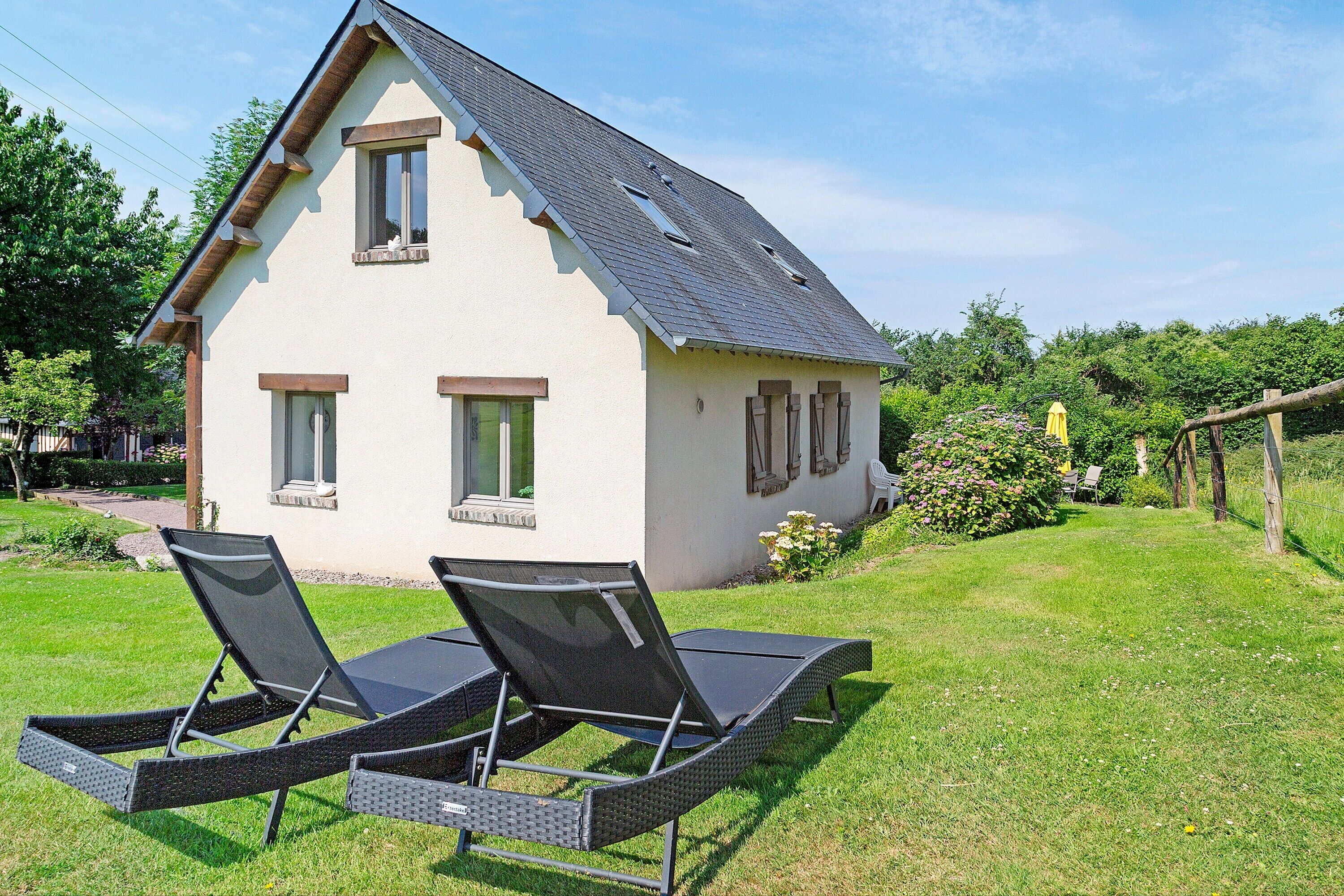 A two-story house with a sloped roof, a small porch, and a lawn with two sun loungers.