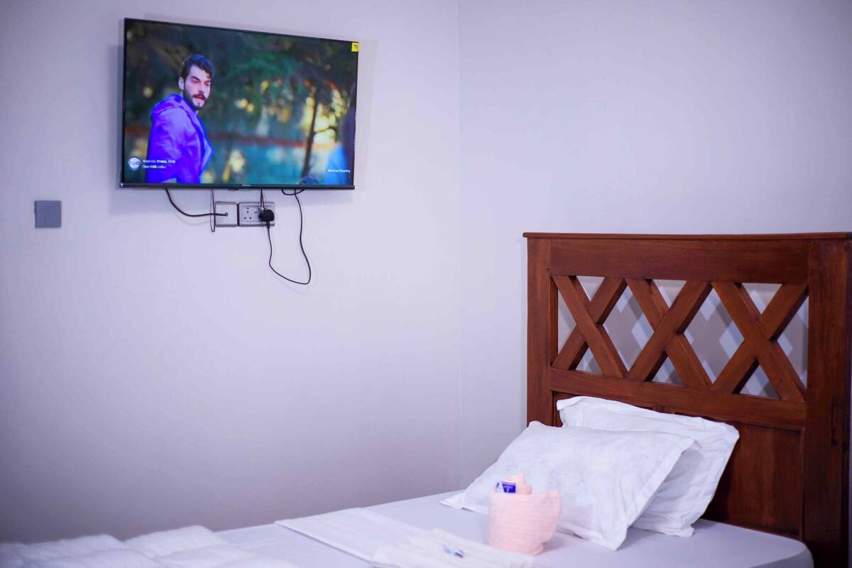 Une chambre d’hôtel avec un lit, une tête de lit en bois, un téléviseur fixé au mur et une prise de courant.