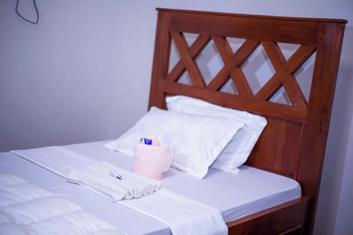 Un lit bien fait, avec des draps blancs, une tête de lit en bois et un oreiller rose.