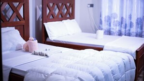 Habitación de hotel con dos camas, cabeceros de madera, ropa de cama blanca y una ventana con cortinas de encaje.
