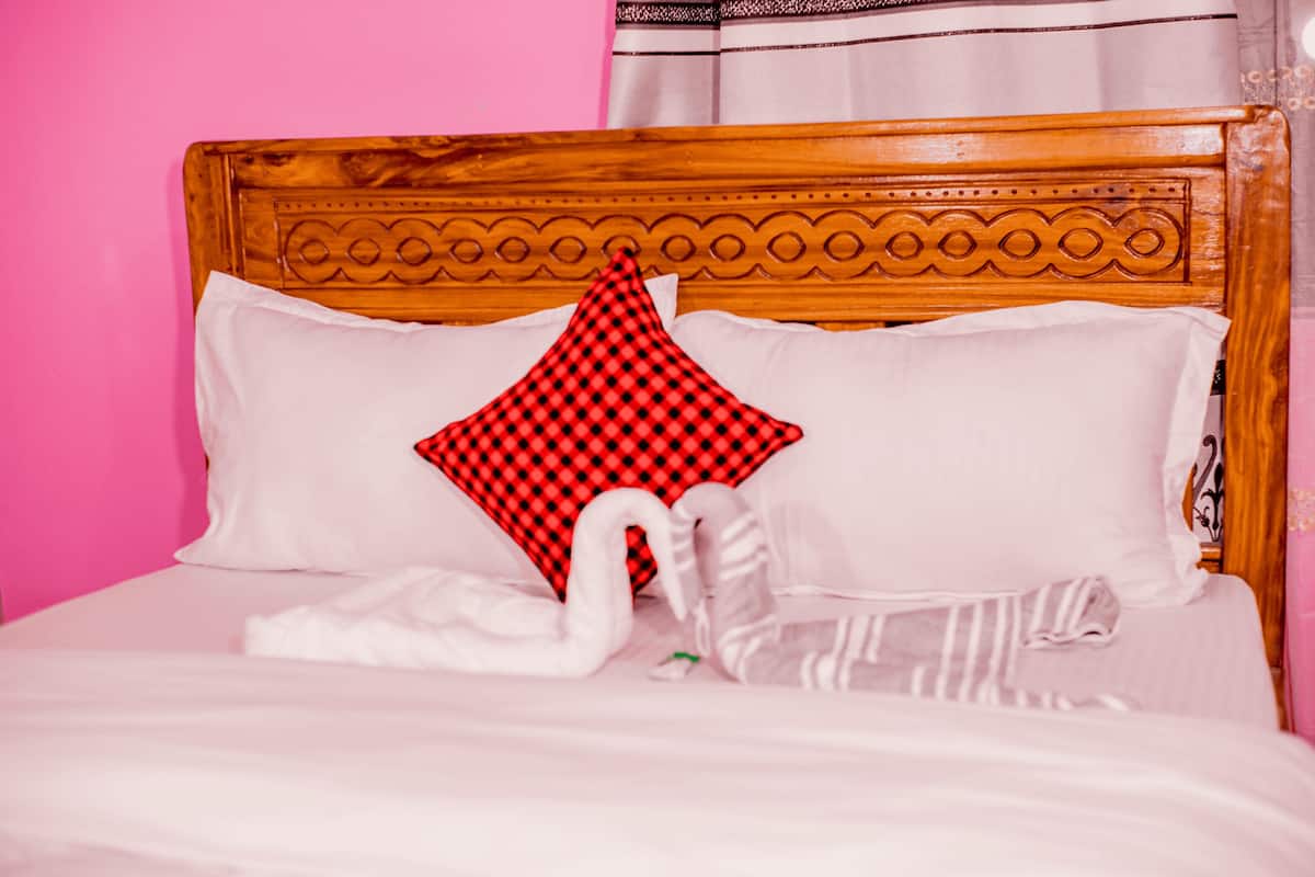 Un lit avec une tête de lit en bois, une literie blanche, un coussin à carreaux rouges et noirs et une décoration en forme de cygne blanc.