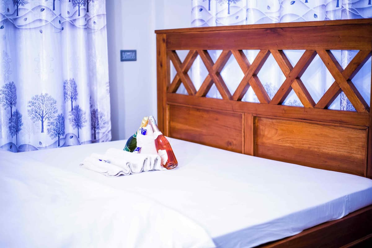 Un lit avec une tête de lit en bois, du linge de lit blanc et une bouteille d’eau posée sur le lit.