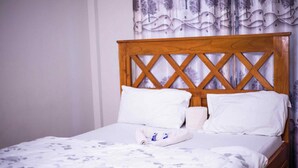 Una cama bien tendida con cabecera de madera, ropa de cama blanca y una manta estampada con motivos florales.