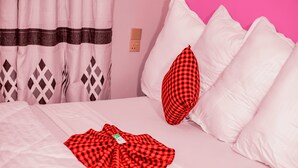Una cama con sábanas blancas, un plaid rojo y blanco, y una almohada con funda a cuadros rojo y negro.