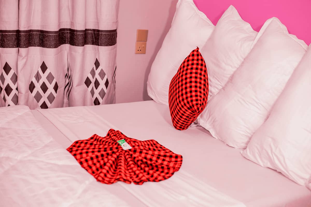 Un lit avec du linge de lit blanc, une couverture à carreaux rouges et un oreiller recouvert d’une housse à carreaux rouges et noirs.