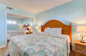 Quarto com duas camas, cabeceira de madeira, mesas de cabeceira com abajures e um espelho.