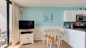 Ein Zimmer mit Fernseher, Esstisch, Stühlen, Küchenzeile und einer Glastür.