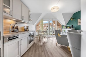 A modern kitchen with a dining area, a sofa, and a view of the outside. - Kronsgaard Beach Loft - Ocean View, Activity Room, Playground, Balcony (Kronsgaard)