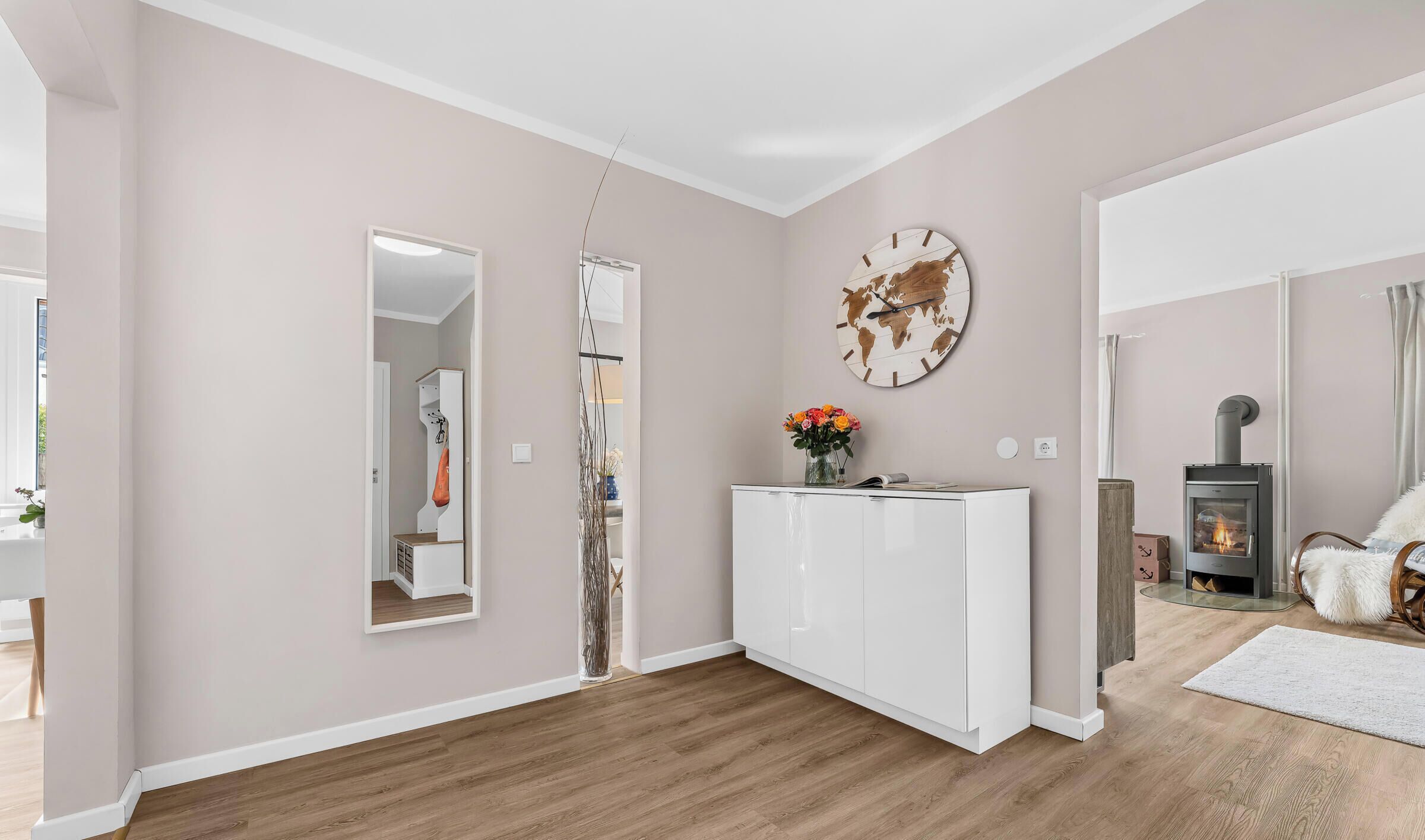 Un salon moderne avec une console blanche, une horloge en forme de carte du monde, une cheminée et un miroir.