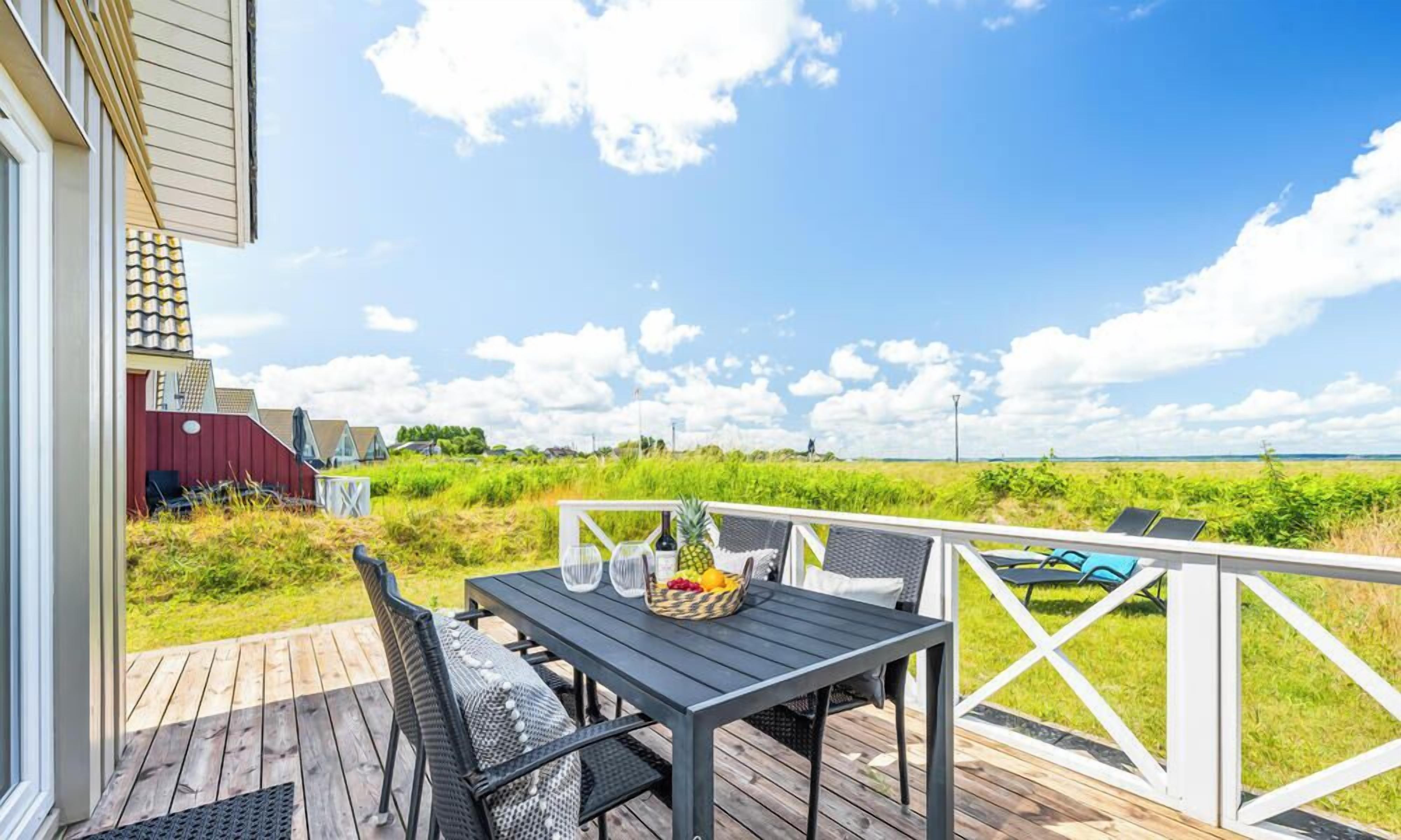 A deck with a table and chairs, a fruit bowl, and a view of the beach.