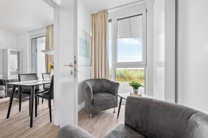Ein modernes Zimmer mit Essbereich, einem grauen Sessel und Blick ins Freie.