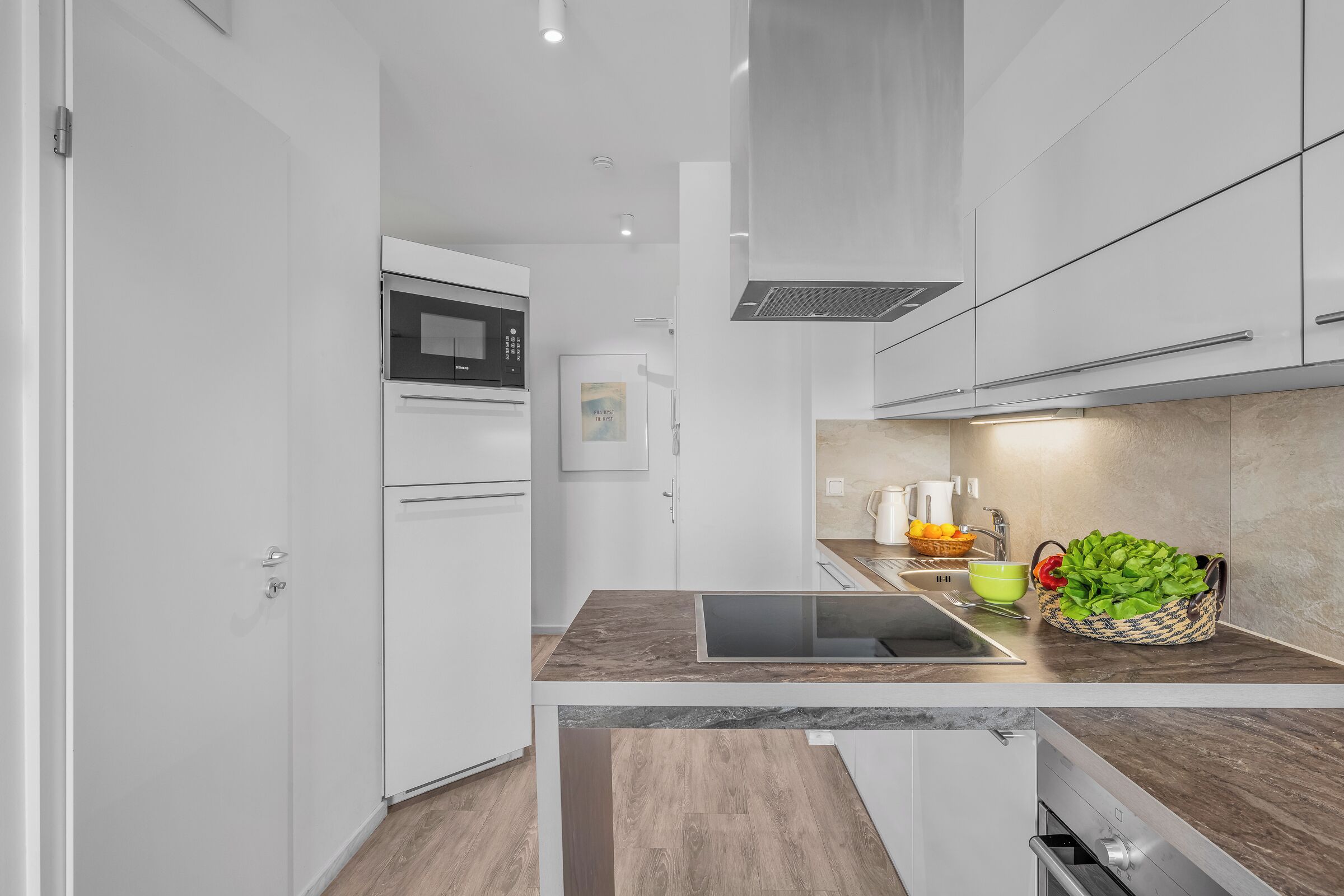 Una cocina moderna con armarios blancos, microondas integrado y campana extractora de acero inoxidable.