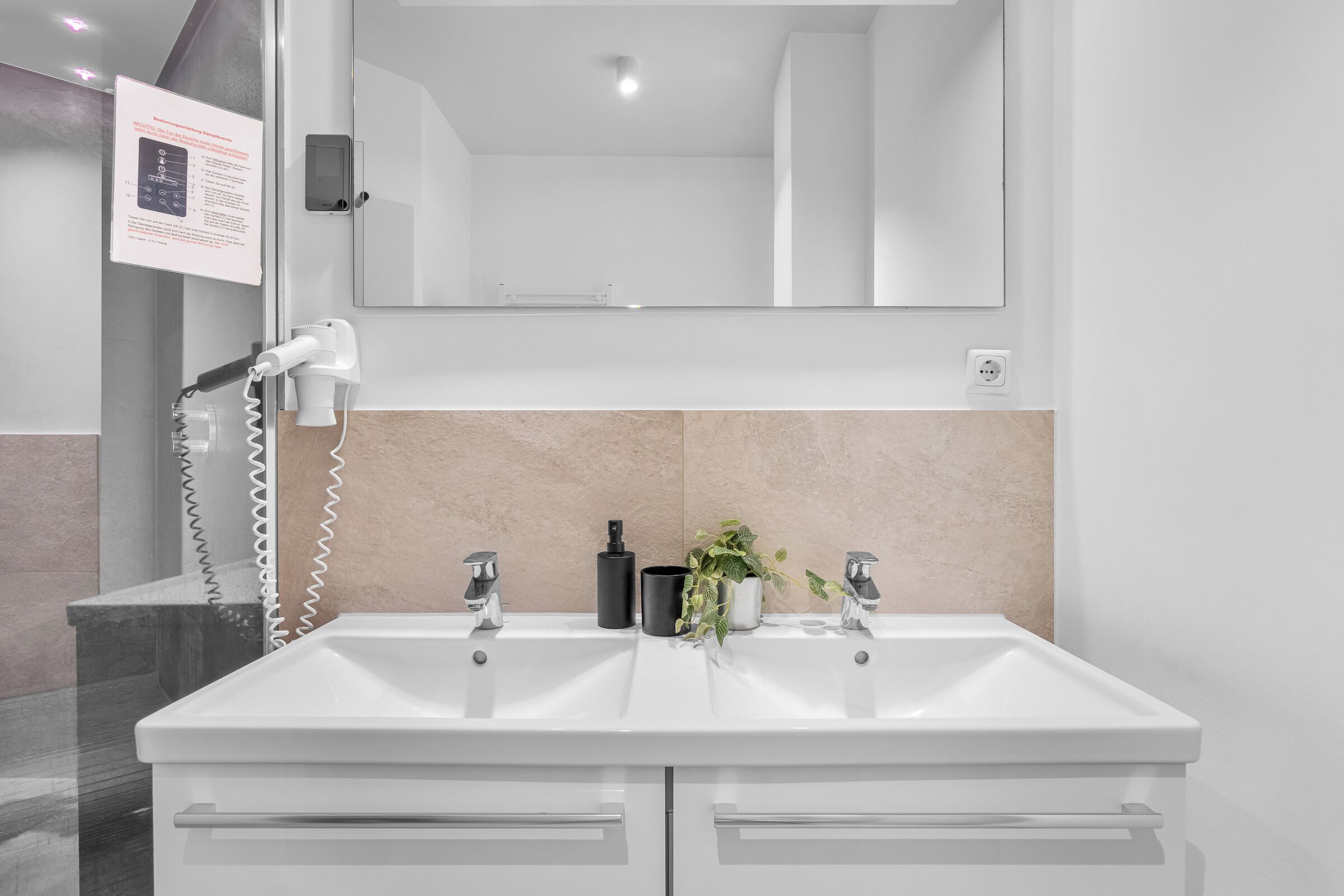A modern bathroom with a dual sink vanity, a handheld hair dryer, and a mirror above the sink.