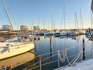 Eine Marina mit mehreren Segelbooten an den Liegen, ruhigem Wasser und Gebäuden im Hintergrund.