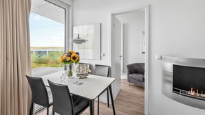 Ett modernt matområde med ett vitt bord, svarta stolar och en vas med blommor.