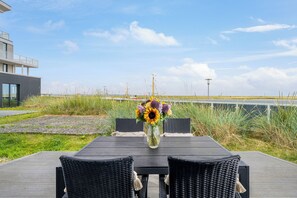 A deck with a table and chairs, a vase of flowers, and a view of the sea and sky. - Spacious Apartment with exceptional Sea View and Wellness Area! (Wendtorf)