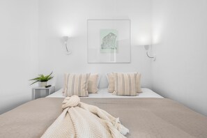 A minimalist bedroom with a bed, pillows, a blanket, a wall-mounted light, and a framed picture. - Spacious Apartment with exceptional Sea View and Wellness Area! (Wendtorf)