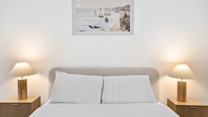 A bedroom with a bed, two bedside tables, and a framed picture of a coastal scene. - Bright 1-bed Stay Near Crown Melbourne (Melbourne)