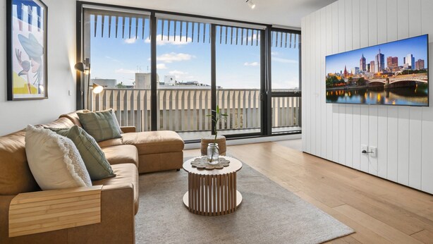 A modern living room with a sofa, a round coffee table, and a large window with a cityscape view. - Bright 1-bed Stay Near Crown Melbourne (Melbourne)