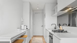 A modern kitchen with white cabinetry, a gas stove, a coffee maker, and wooden bar stools. - Bright 1-bed Stay Near Crown Melbourne (Melbourne)