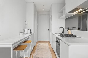 Eine moderne Küche mit weißen Schränken, einem Gasherd, einer Kaffeemaschine und Holzbarhocker.