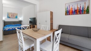 A modern room with a dining table, white chairs, a grey sofa, a TV, and a cabinet. - Apartment 'Casa Leone' with Air Conditioning (Teulada)
