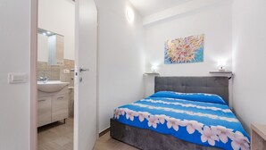 A bedroom with a bed, a nightstand, a wall-mounted lamp, a painting, and a bathroom visible through an open door. - Apartment 'Casa Leone' with Air Conditioning (Teulada)