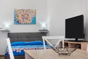 Et soveværelse med seng, fjernsyn, et maleri og et skrivebord med stol.