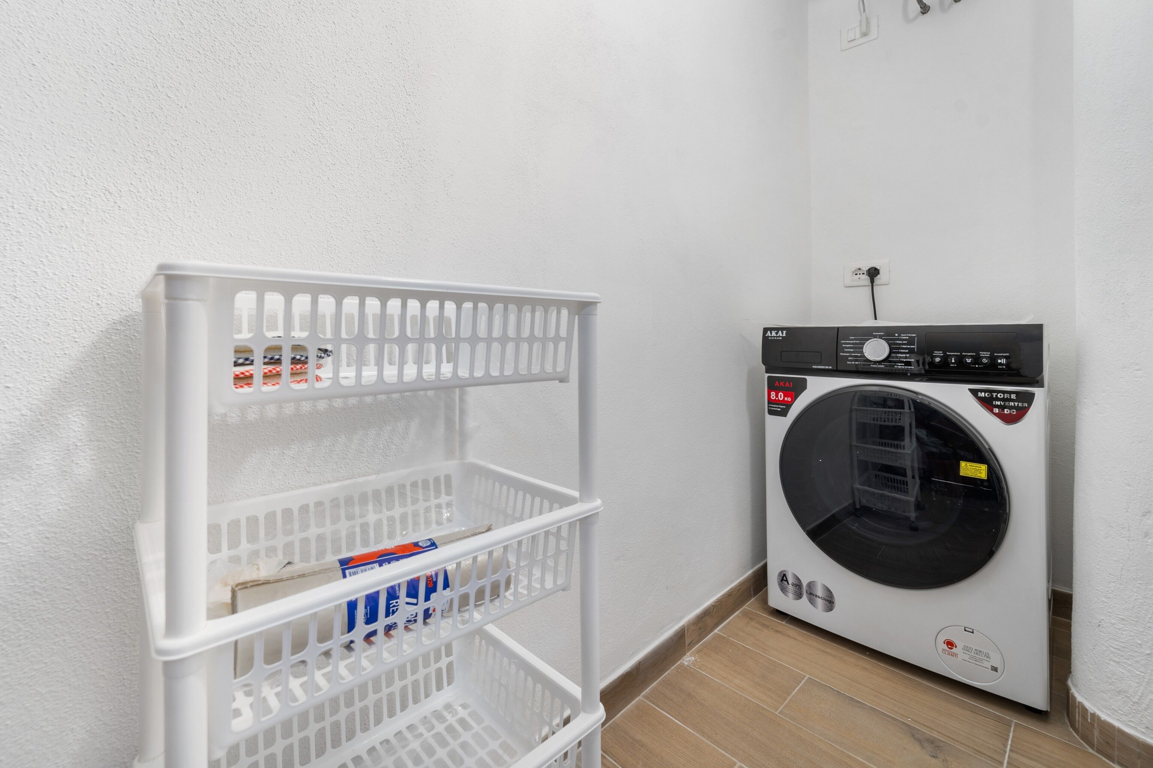 Un espace buanderie avec un lave-linge blanc et une étagère en plastique blanche, sur laquelle sont posés divers objets.