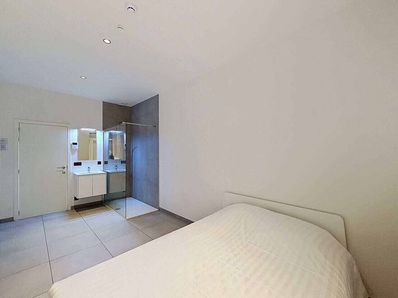 Een slaapkamer met een bed, een badkamer met een spiegel en een deur.