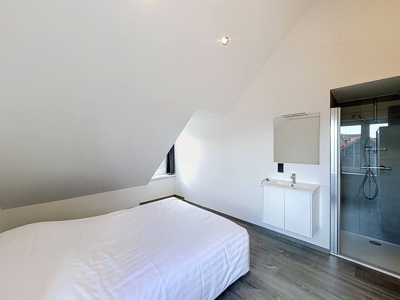 A bedroom with a bed, a white dresser, a mirror, and a glass shower enclosure.