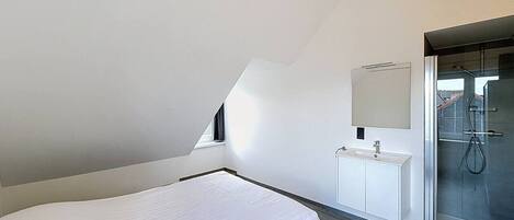 A bedroom with a bed, a white dresser, a mirror, and a glass shower enclosure.