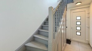 Eine Treppe mit weißen Stufen und einem hölzernen Geländer, die zu einer Tür mit einer Lampe darüber führt.