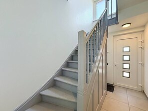 Eine Treppe mit weißen Stufen und einem hölzernen Geländer, die zu einer Tür mit einer Lampe darüber führt.