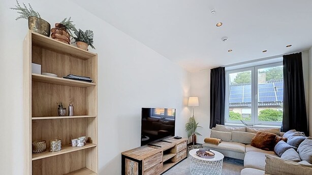 Ein modernes Wohnzimmer mit einer Holztrenneinrichtung, einem Flachbildfernseher, einer Couch, einem Couchtisch und einem großen Fenster mit Vorhängen.