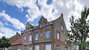 Ein mehrstöckiges Backsteingebäude mit Satteldach, Garage und Parkplatz für zwei Autos.
